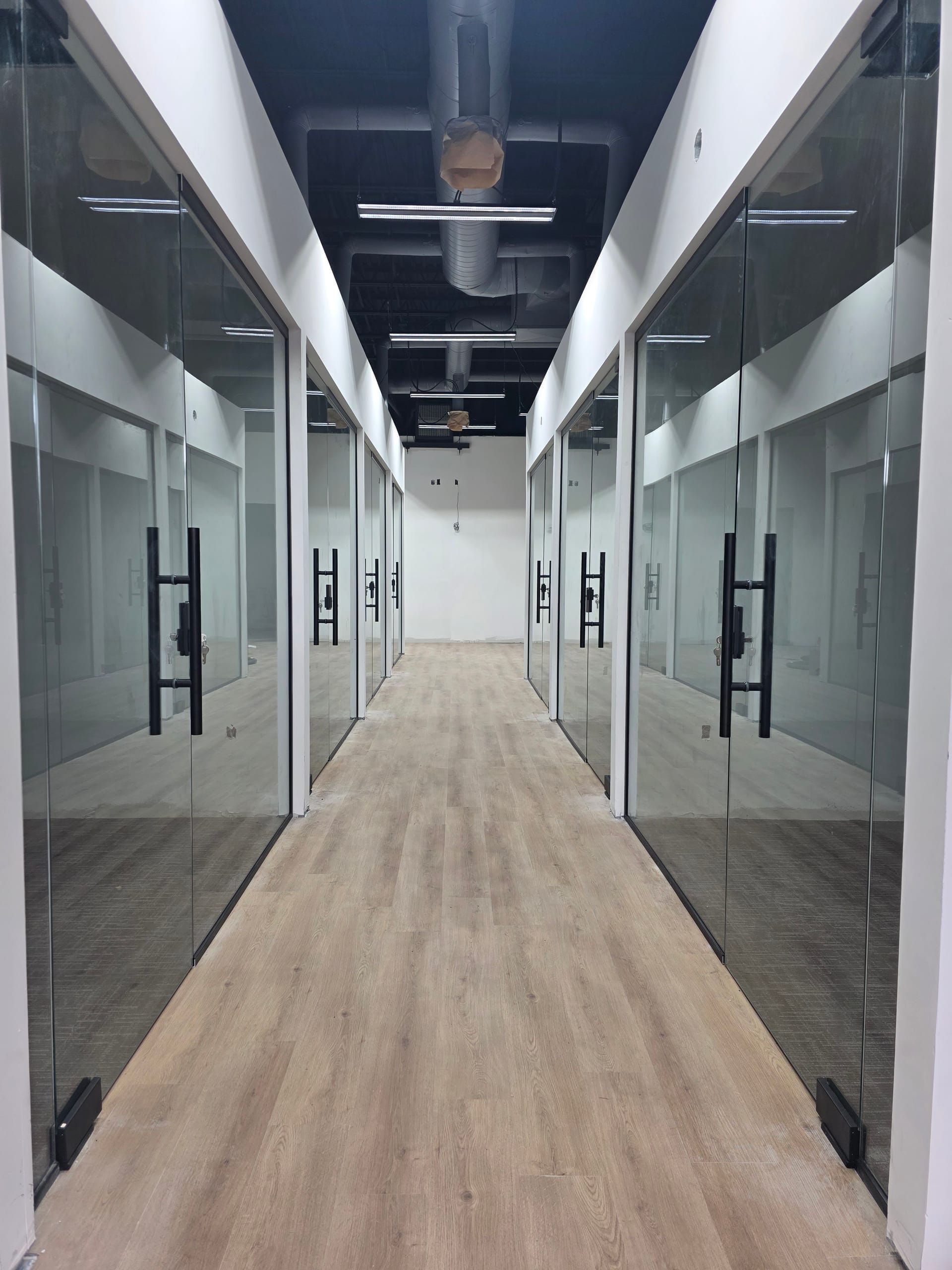 Black frame glass office corridor partition with polished floor and wood accent wall in commercial interior — Built By Glass, Mississauga GTA