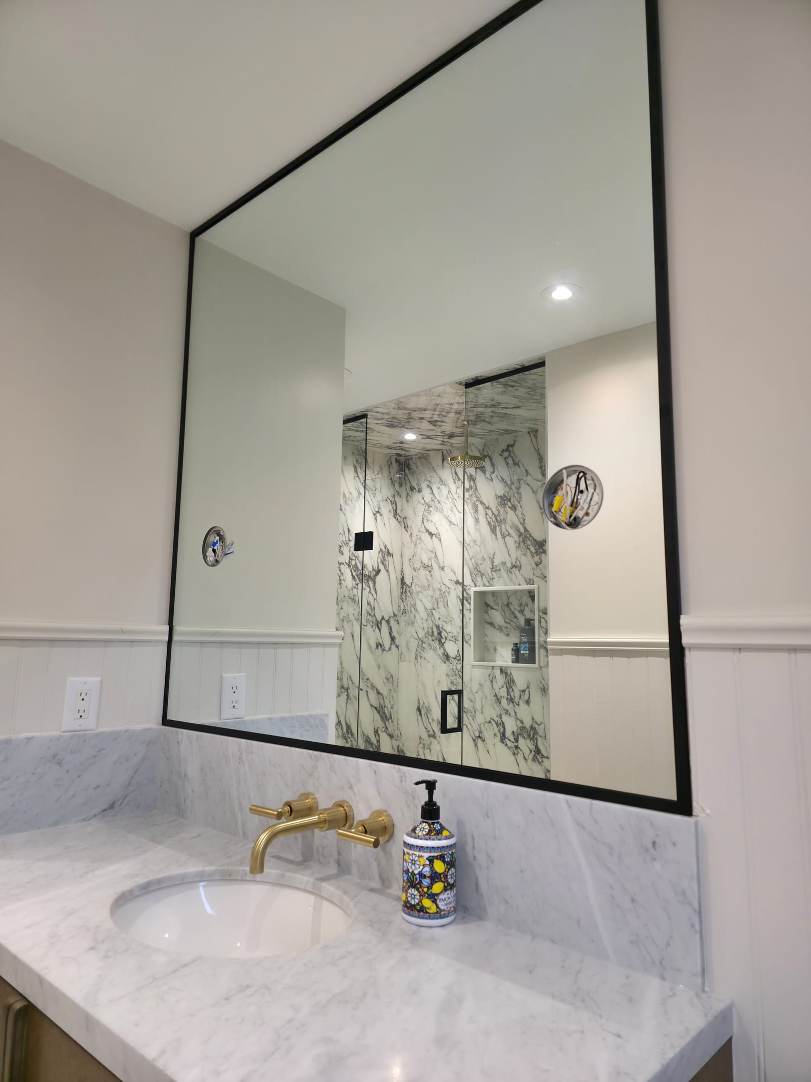 Black-frame custom vanity mirror in a marble bathroom — Built By Glass