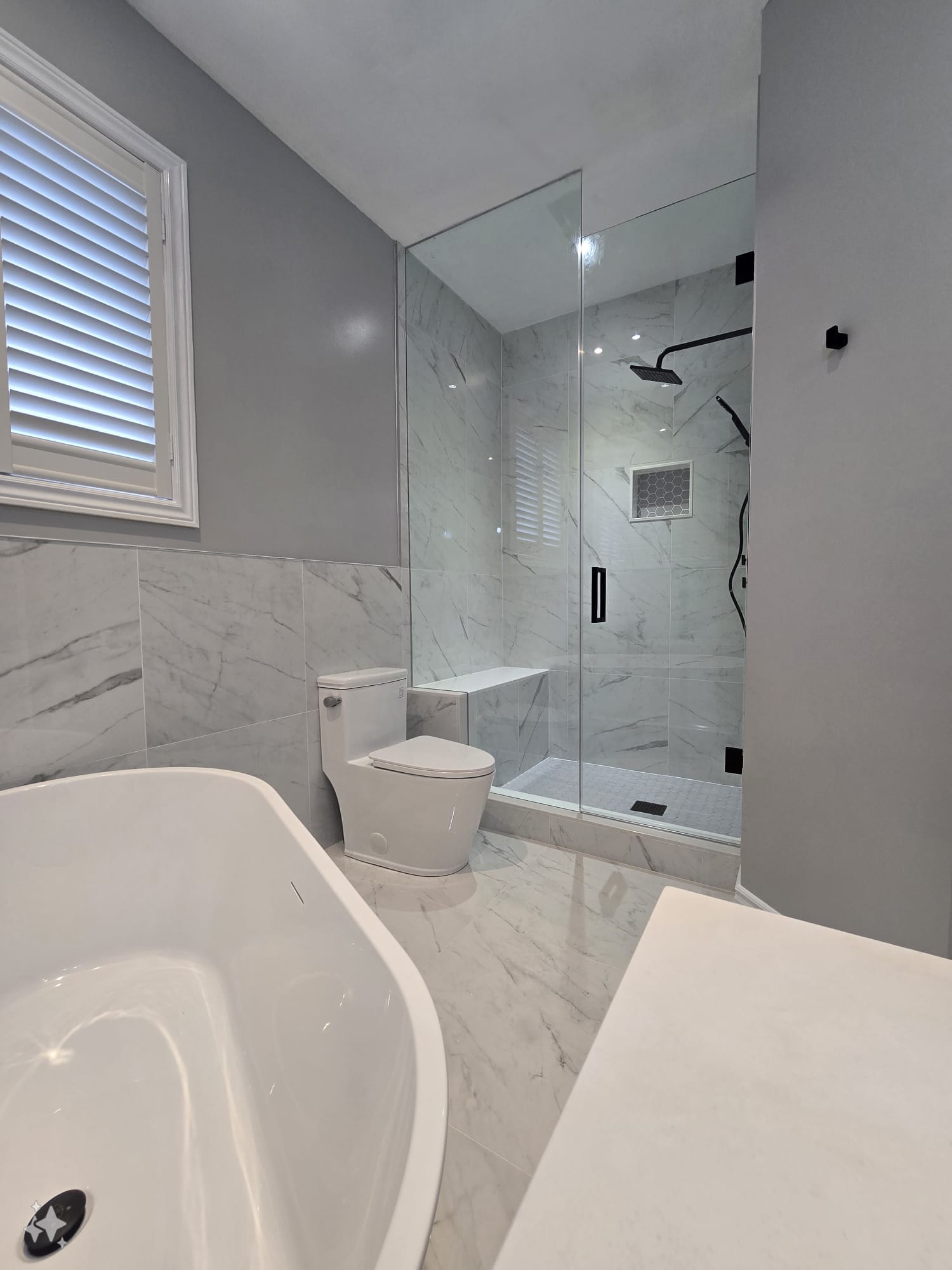Frameless glass shower with black fixtures beside a freestanding soaker tub — Built By Glass